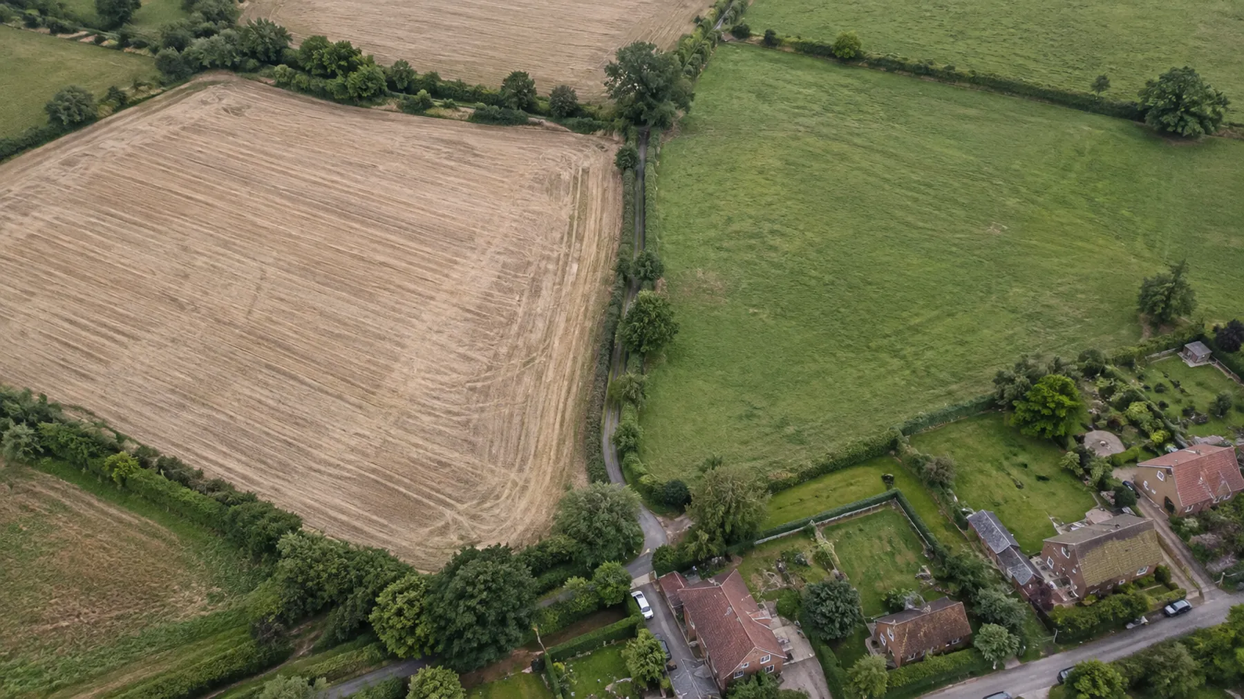 Aerial view of a stubble field and pasture at the edge of a Hertfordshire village